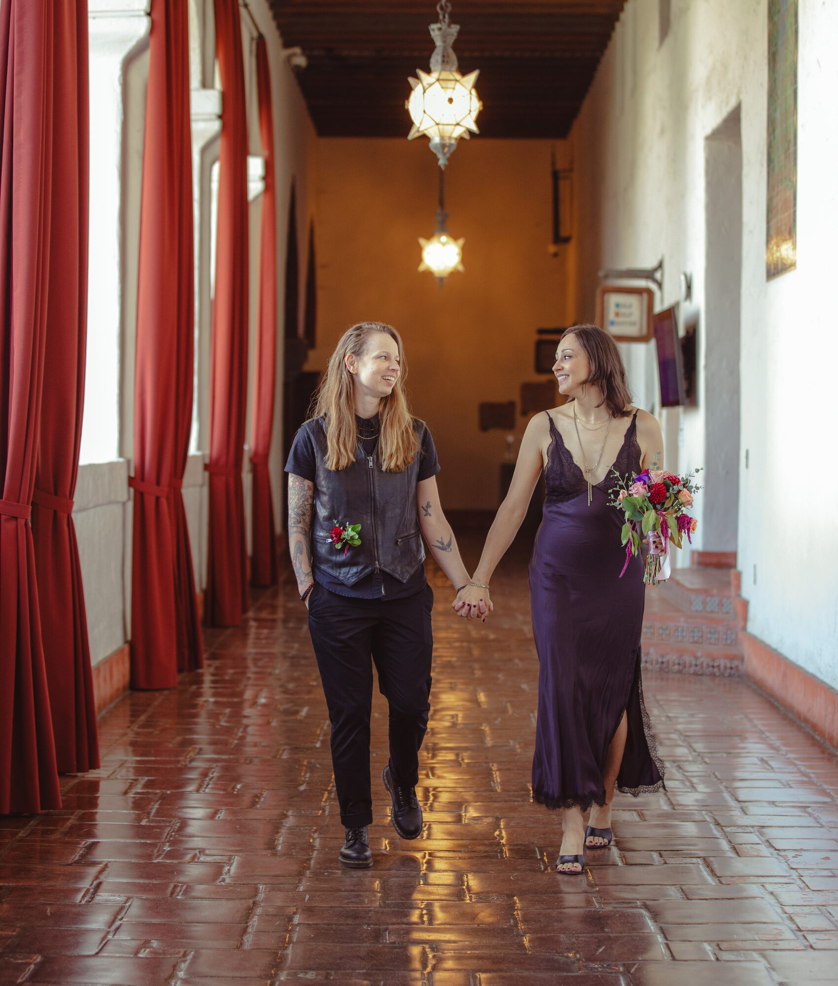 A couple walking hand in hand down a red-curtained mission corridor